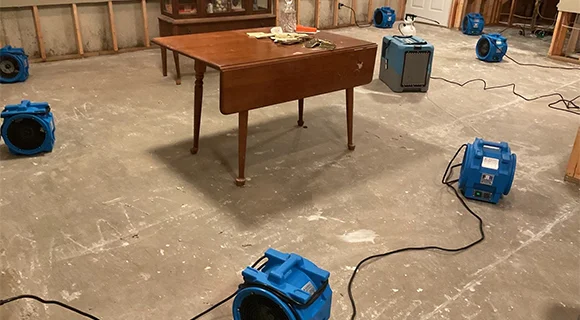 Room with blue dehumidifiers, table, and text about licensed team restoring property safely.